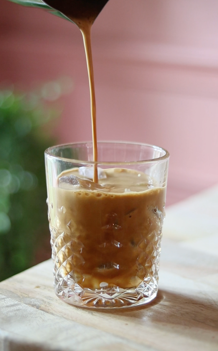 Coffee being poured into a glass on a wooden surface with a blurred background